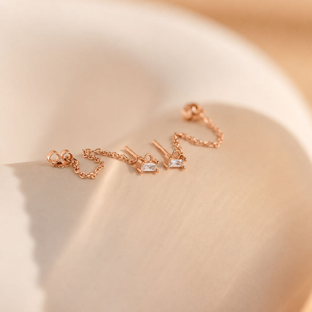 Rose gold jewelry set with chain and small pendants on a beige background