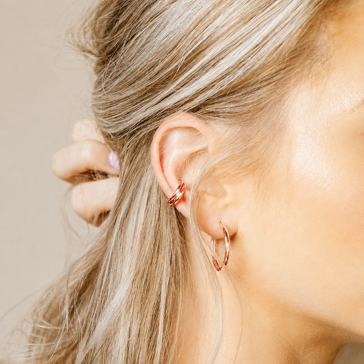 Close-up of a person wearing rose gold hoop earrings with a neutral background