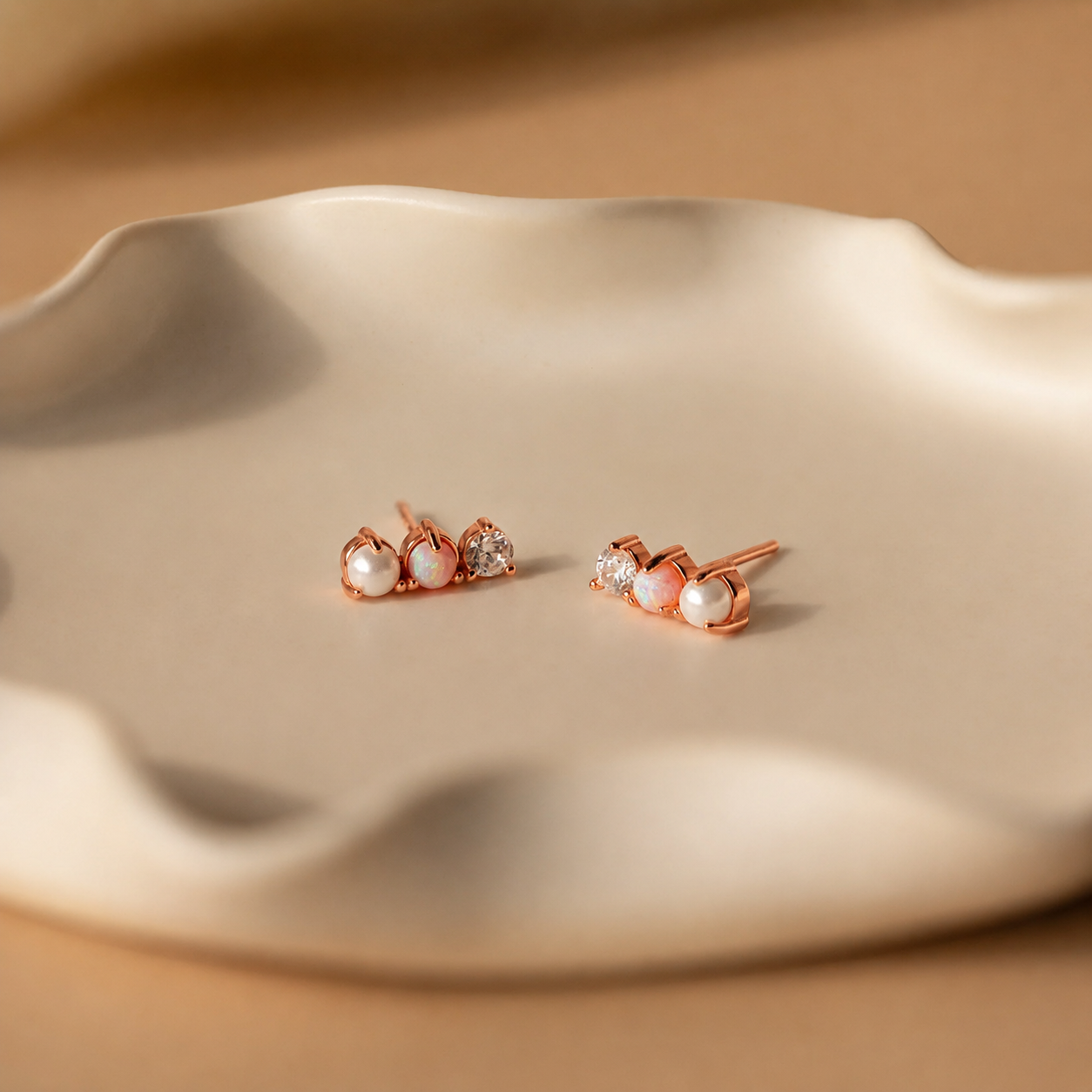 Rose gold earrings with pearls on a beige dish