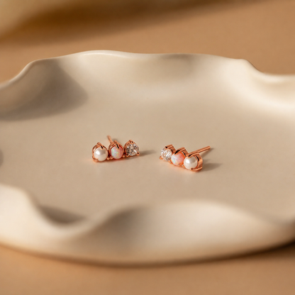 Rose gold earrings with pearls on a beige dish