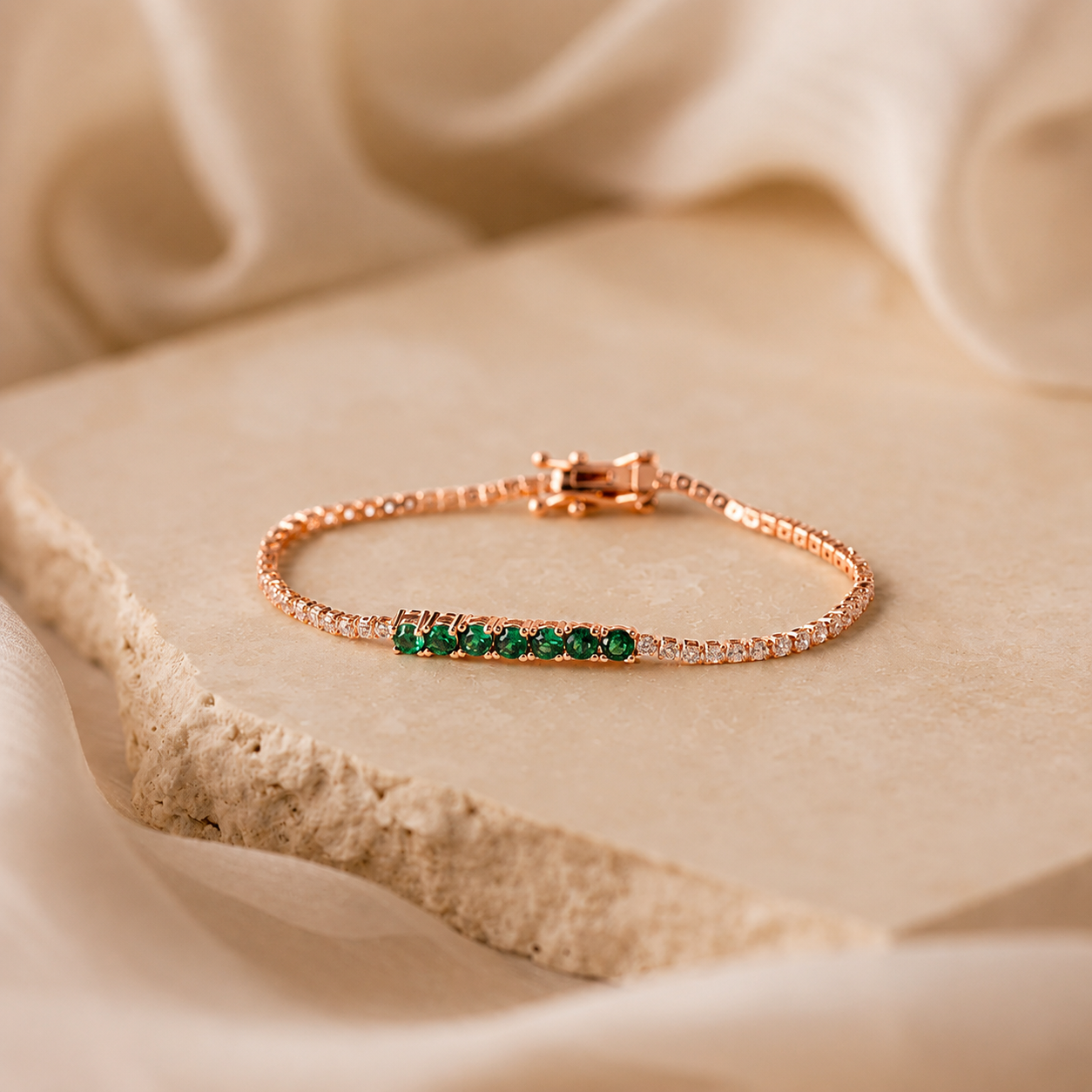 Rose gold bracelet with green gemstones on a beige fabric background