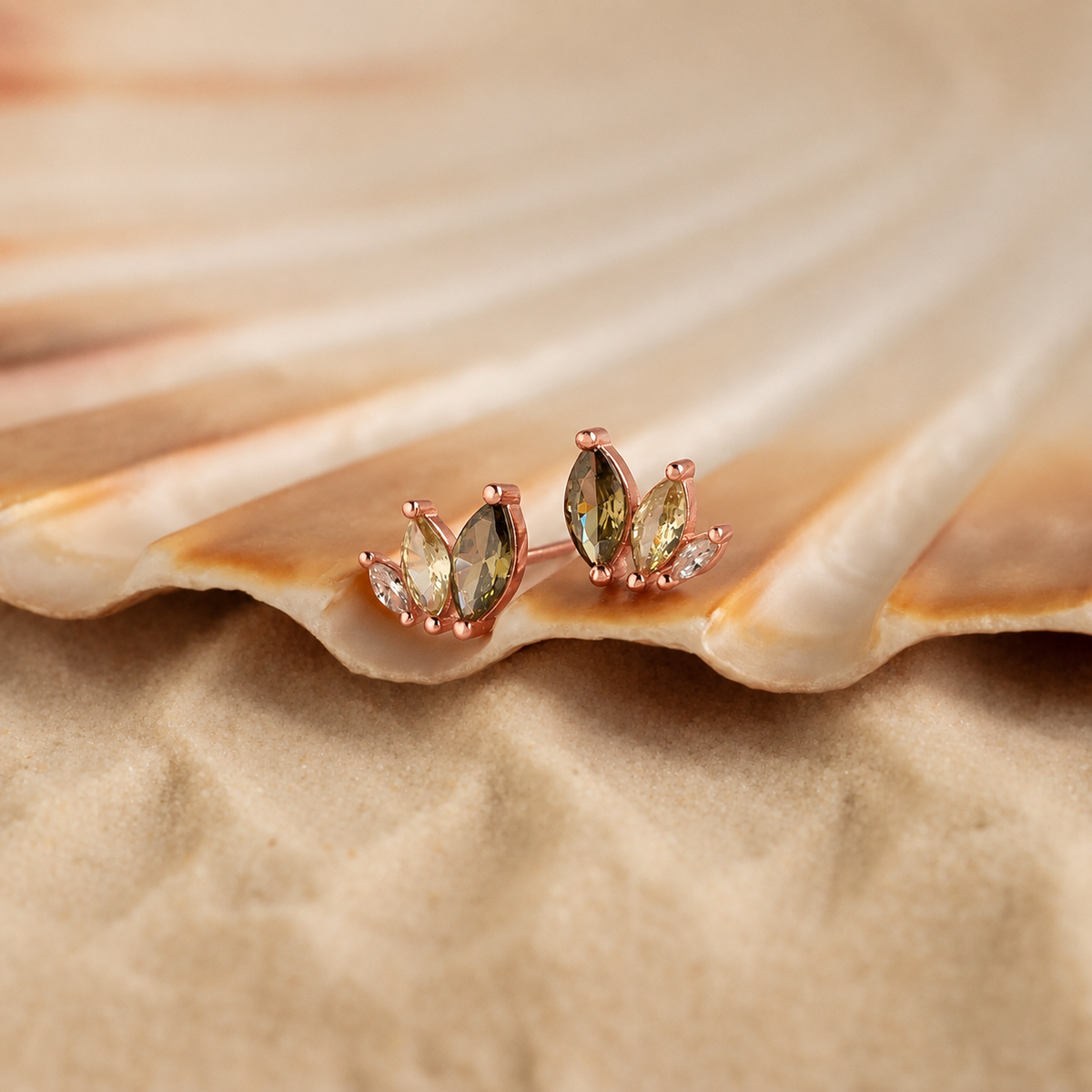 Pair of rose gold earrings with green gemstones on a seashell.