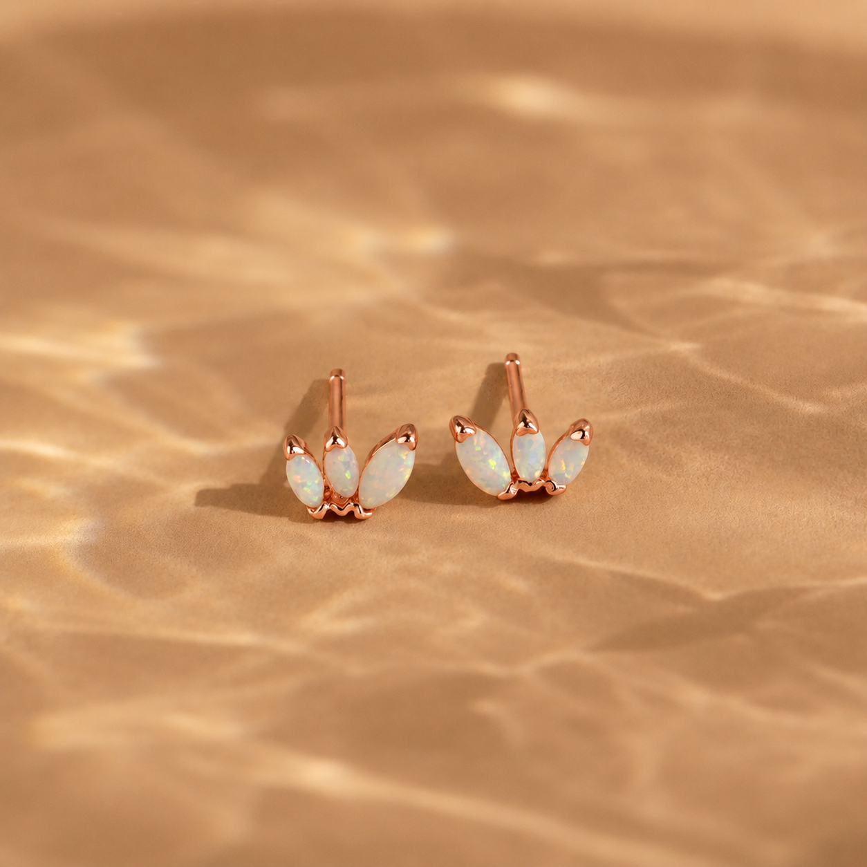 Rose gold earrings with opal stones on a beige fabric background