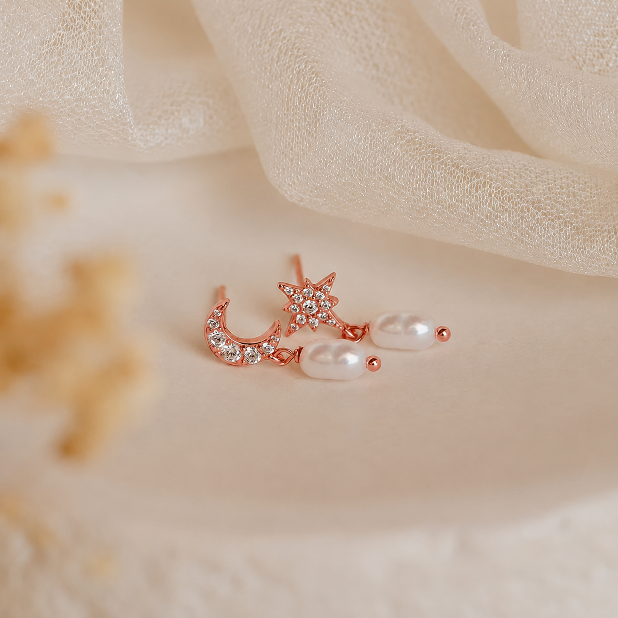Rose gold earring with star, moon, and pearl design on a soft beige fabric background