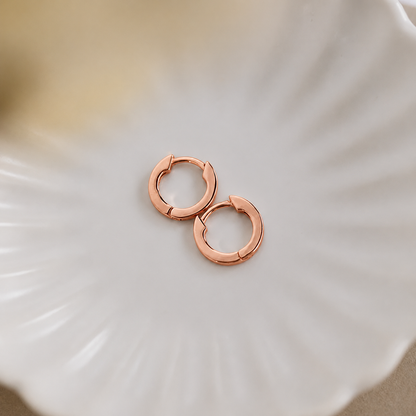 Rose gold hoop earrings on a white shell