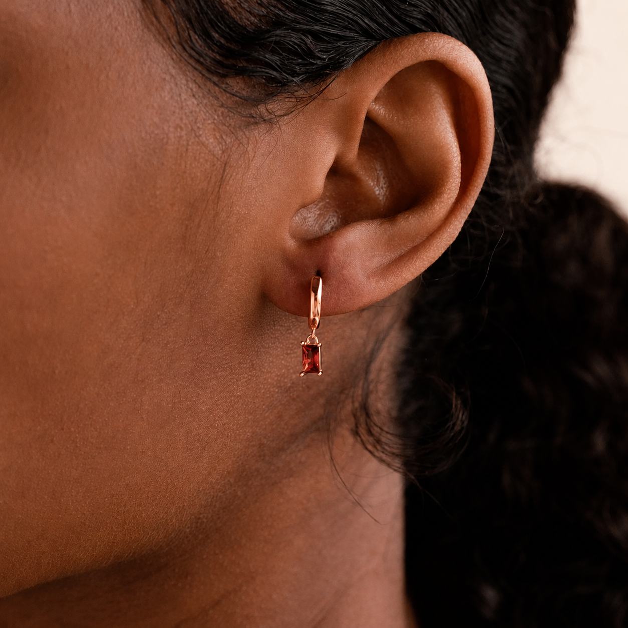 Close-up of an ear wearing a rose gold hoop earring with a red gemstone.