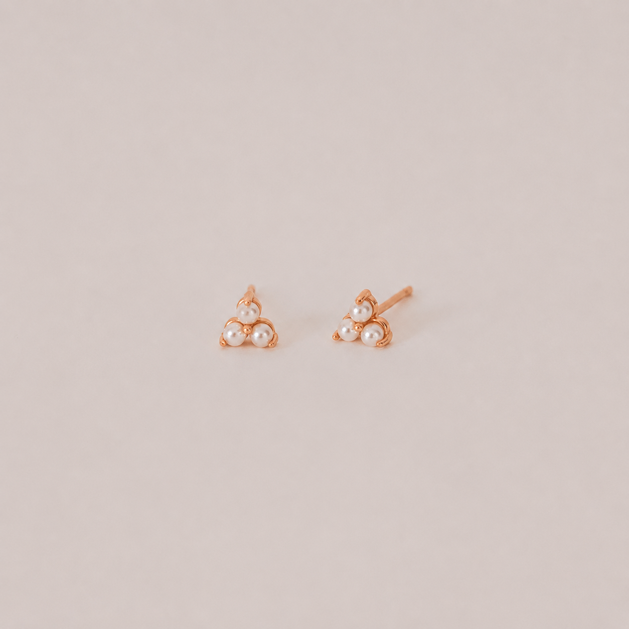 Pair of rose gold earrings with pearl-like stones on a beige background