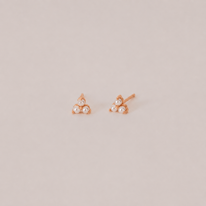 Pair of rose gold earrings with pearl-like stones on a beige background