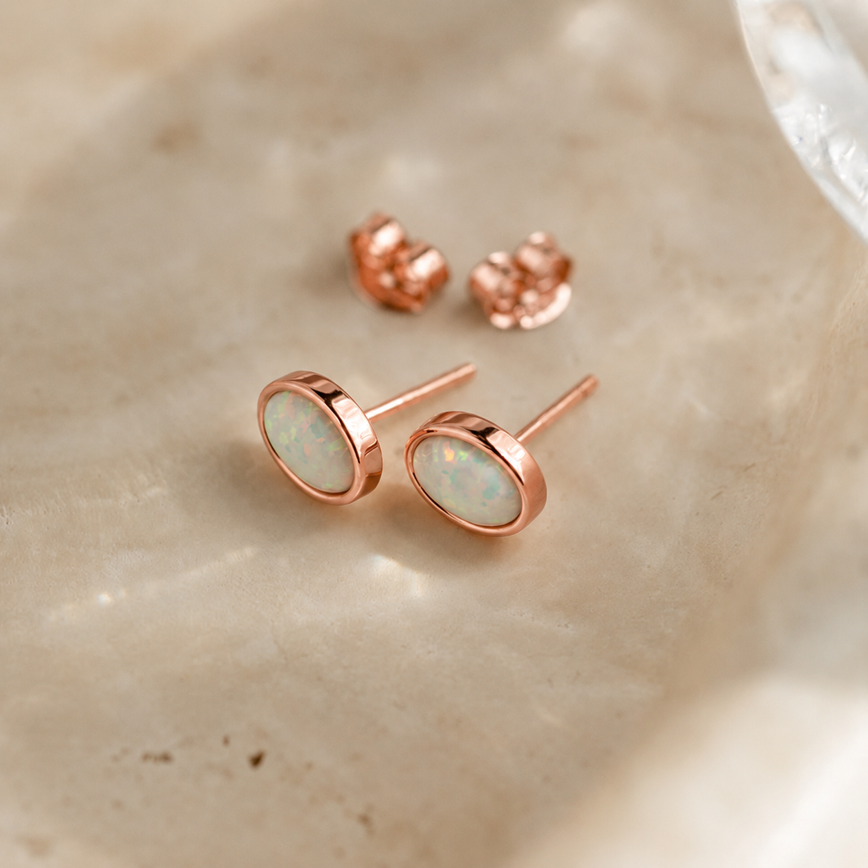 Rose gold earrings with opal stones on a beige surface