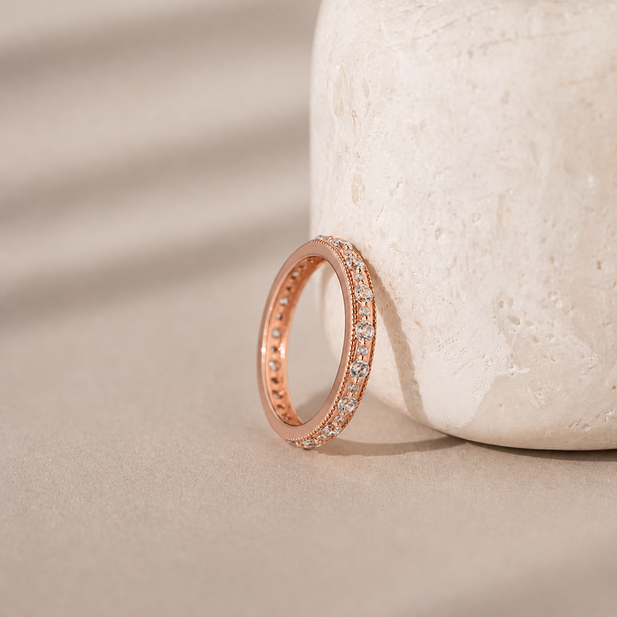 Rose gold ring with diamonds on a beige stone surface