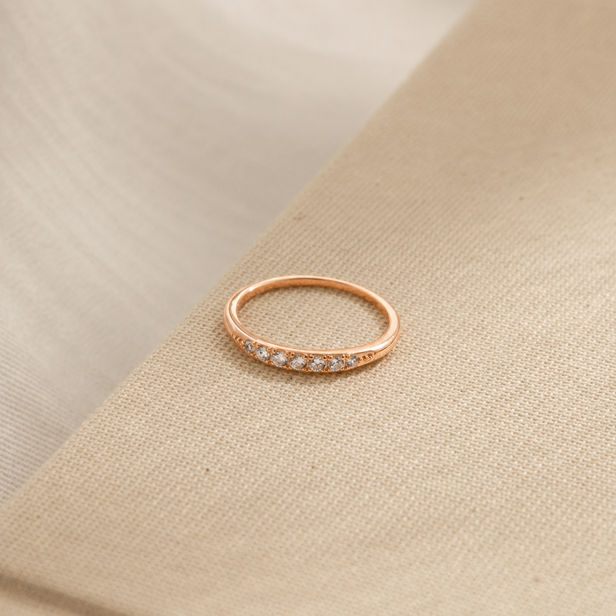 Rose gold ring with small diamonds on a beige fabric background
