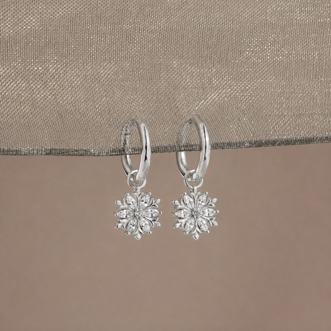 Silver snowflake earrings on a beige fabric background