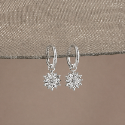 Silver snowflake earrings on a beige fabric background