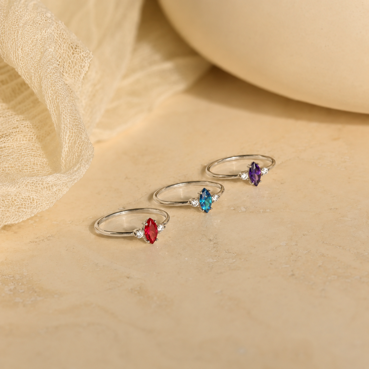 Set of four silver rings with colorful gemstones on a beige fabric background