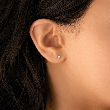 A close-up of a person's ear wearing a small, round stud earring with a clear gemstone in a silver-toned setting.
