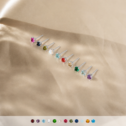 Set of small stud earrings with multicolored gemstones on a beige fabric background