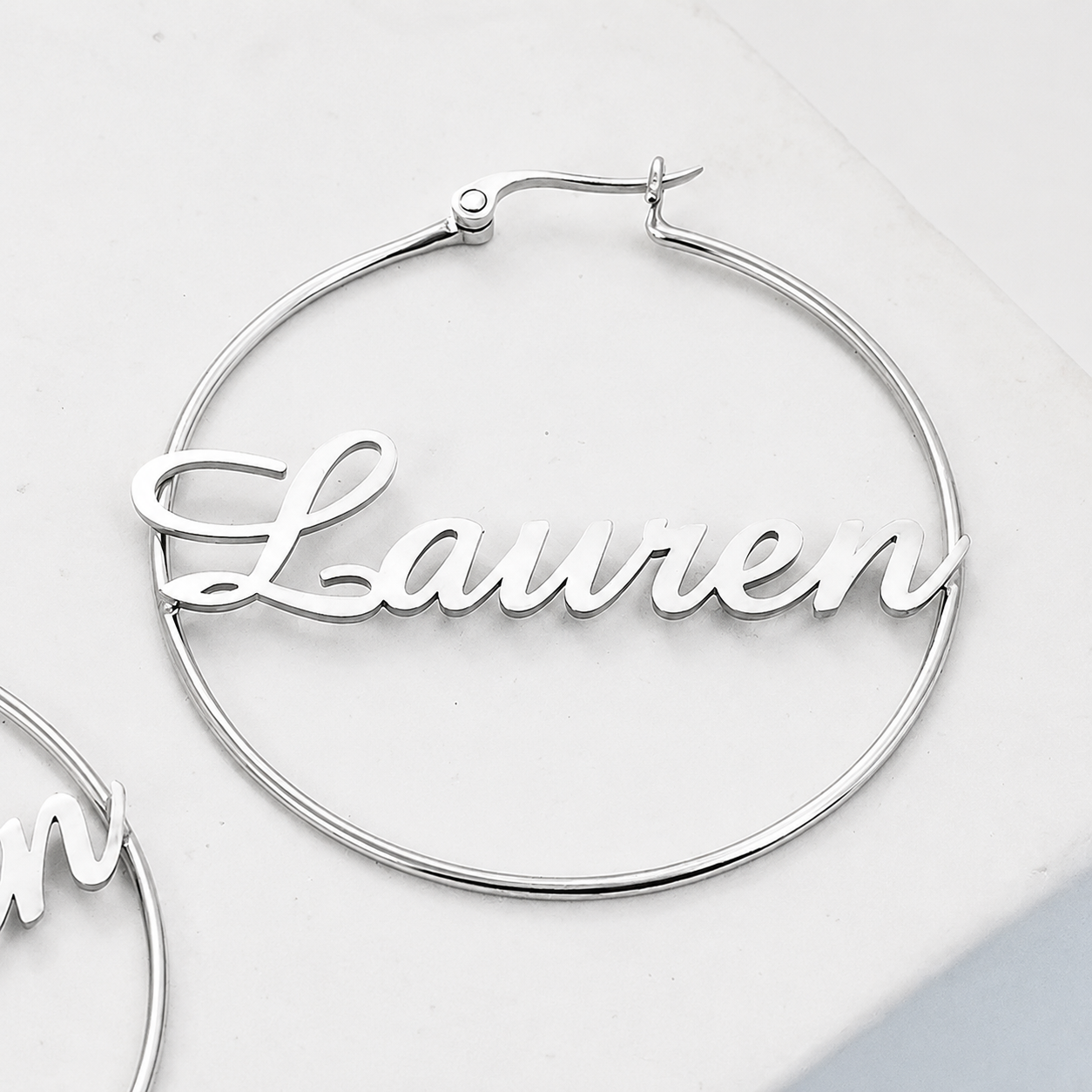 Silver hoop earrings with 'Lauren' engraving on a light gray background