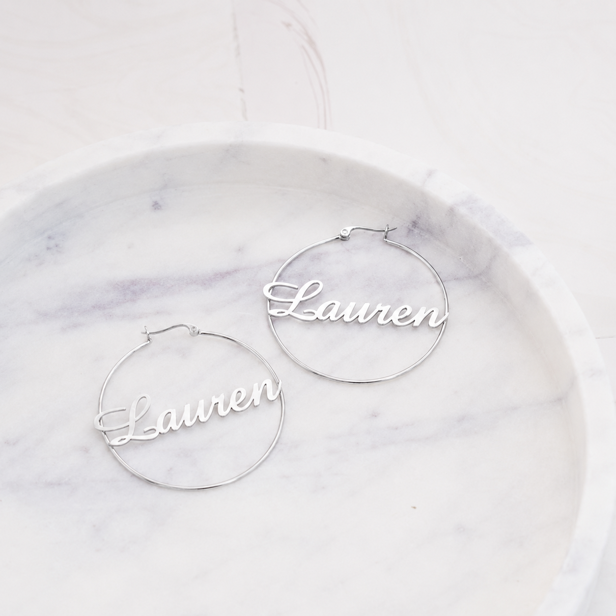 Silver hoop earrings with 'Lauren' engraved on a marble surface