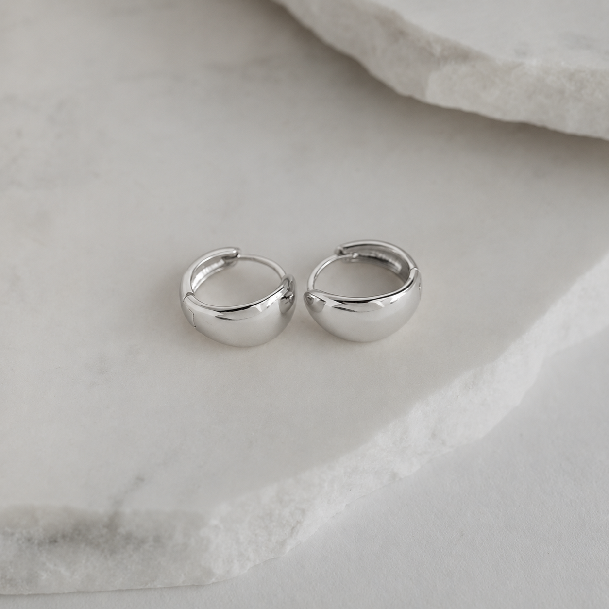 Pair of silver hoop earrings on a marble surface