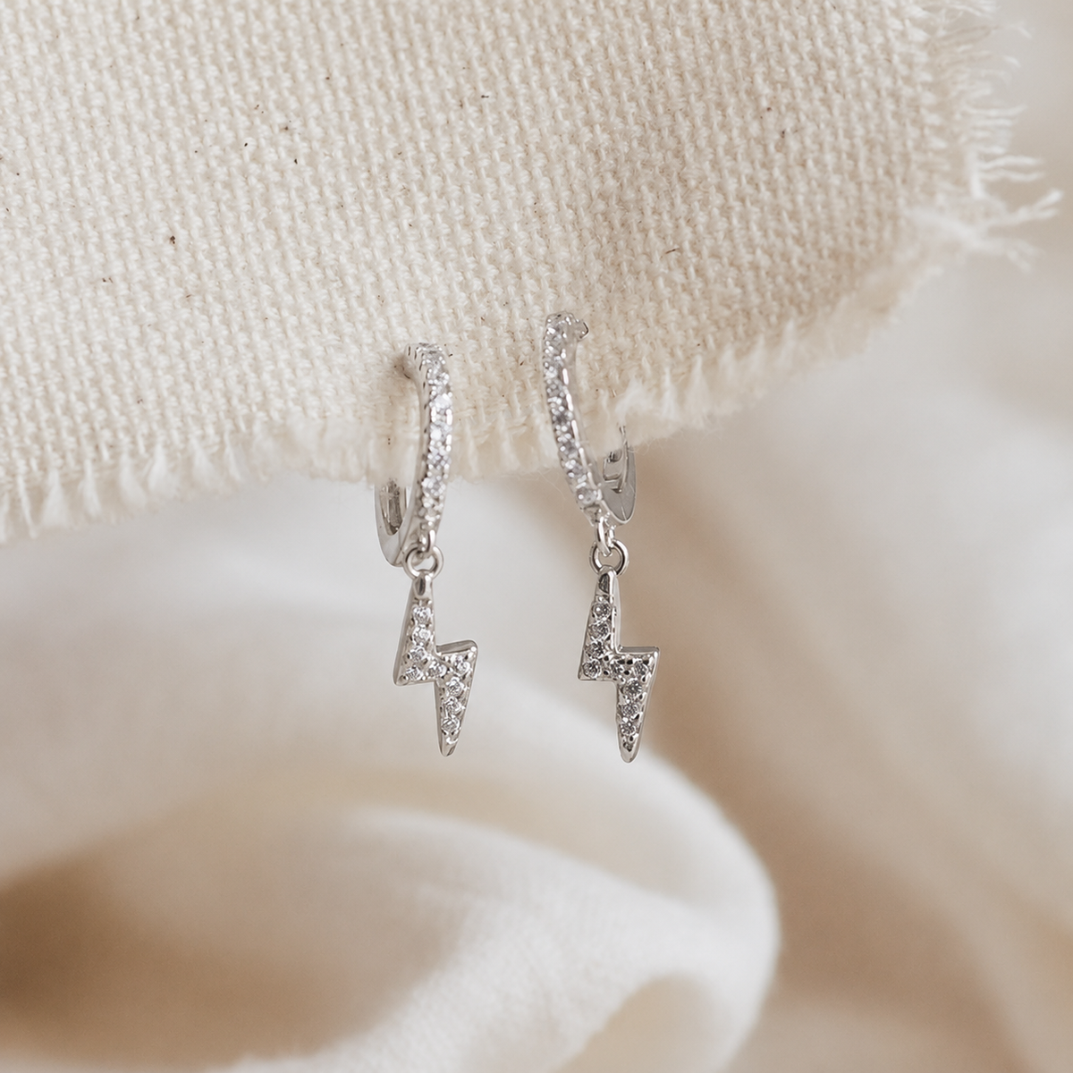 Silver lightning bolt earrings on a textured beige fabric background