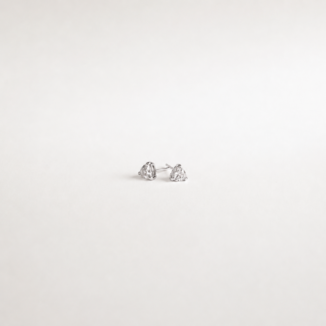 A pair of small silver stud earrings with clear heart-shaped gemstones, photographed on a plain white background.