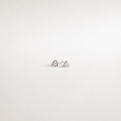 A pair of small silver stud earrings with clear heart-shaped gemstones, photographed on a plain white background.