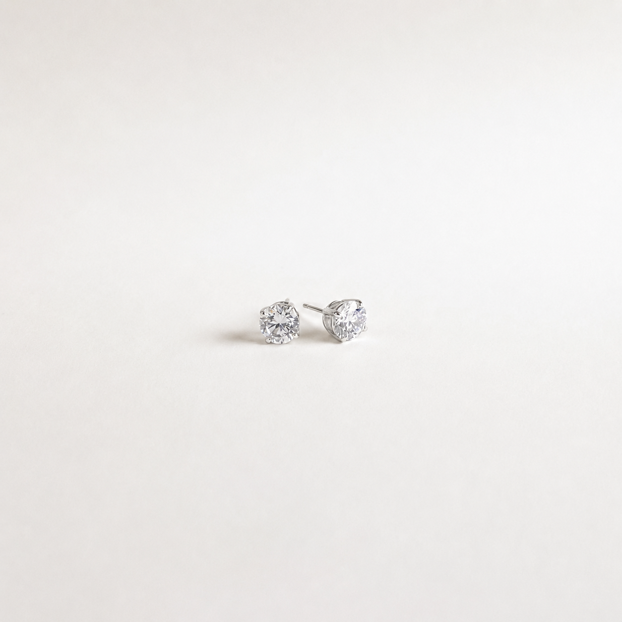 A pair of small silver stud earrings with clear gemstones, photographed on a plain white background.