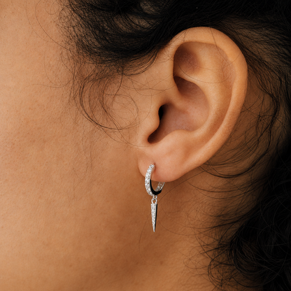 Close-up of an ear wearing a silver hoop earring with a dangling diamond.