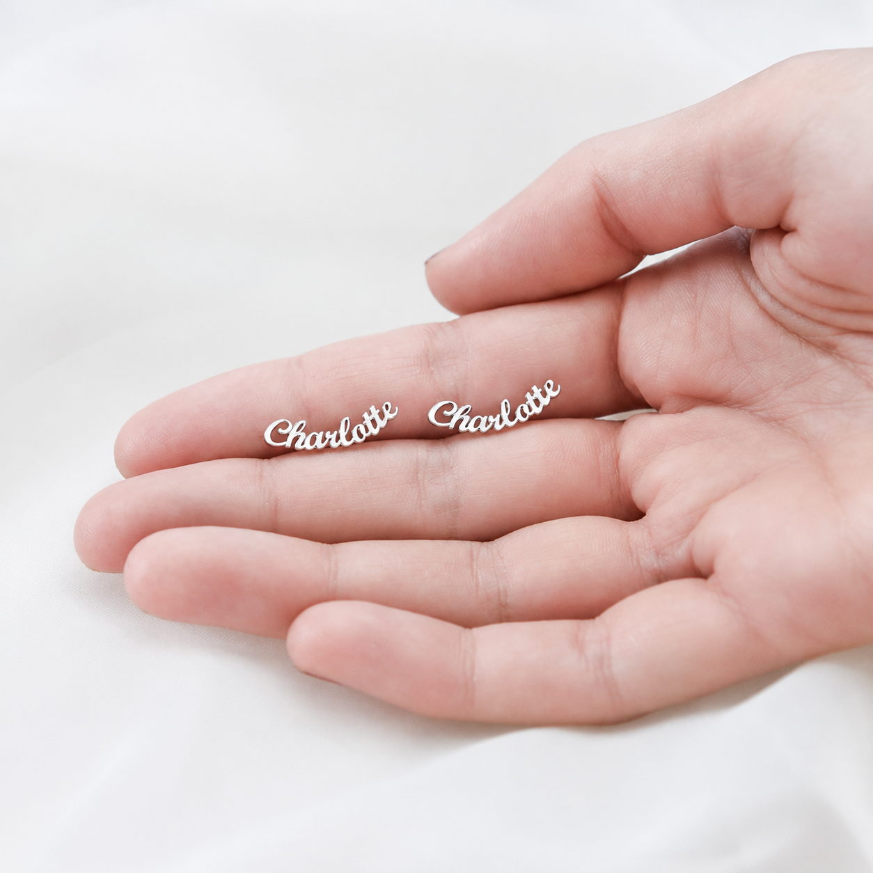 Two silver 'Charlotte' earrings on a hand against a white background