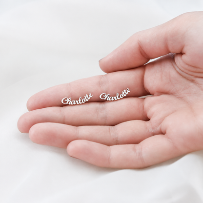 Two silver 'Charlotte' earrings on a hand against a white background