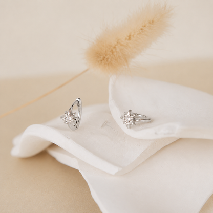 Silver earrings on a white fabric with a soft beige background