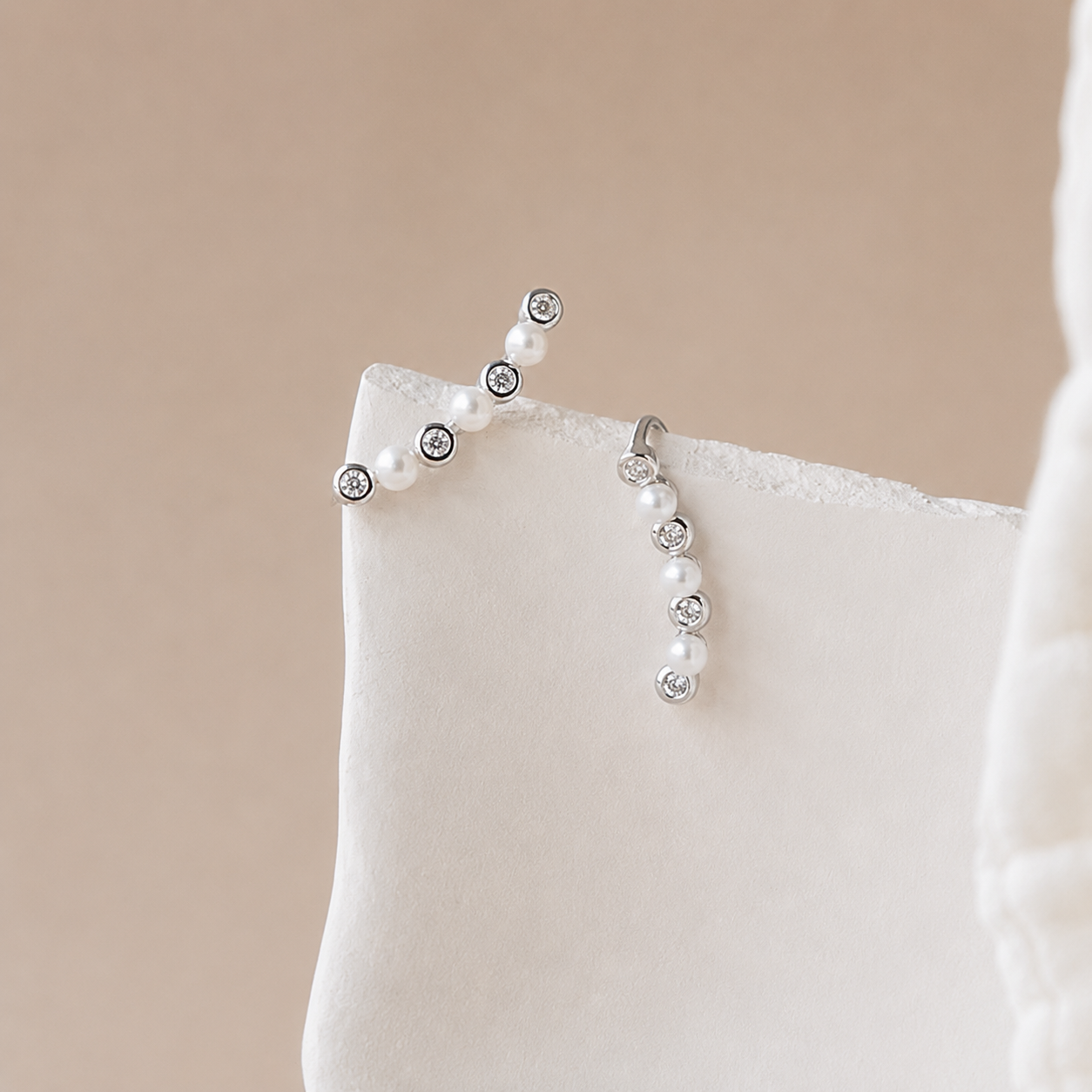 Pearl and crystal earrings on a beige cushion with a neutral background