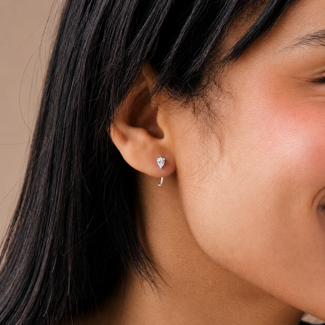 Close-up of a person wearing a silver earring with a clear gemstone.