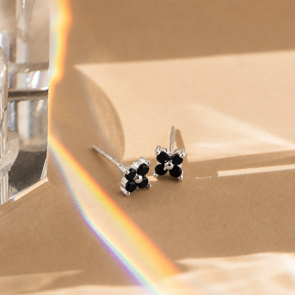 Pair of silver earrings with black stones on a beige surface with a rainbow effect.