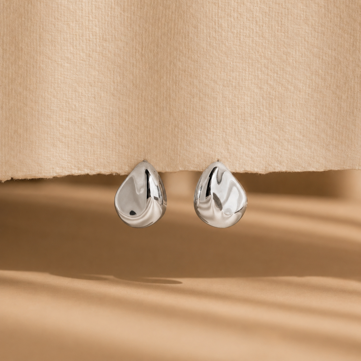 Pair of silver teardrop-shaped earrings on a beige fabric background