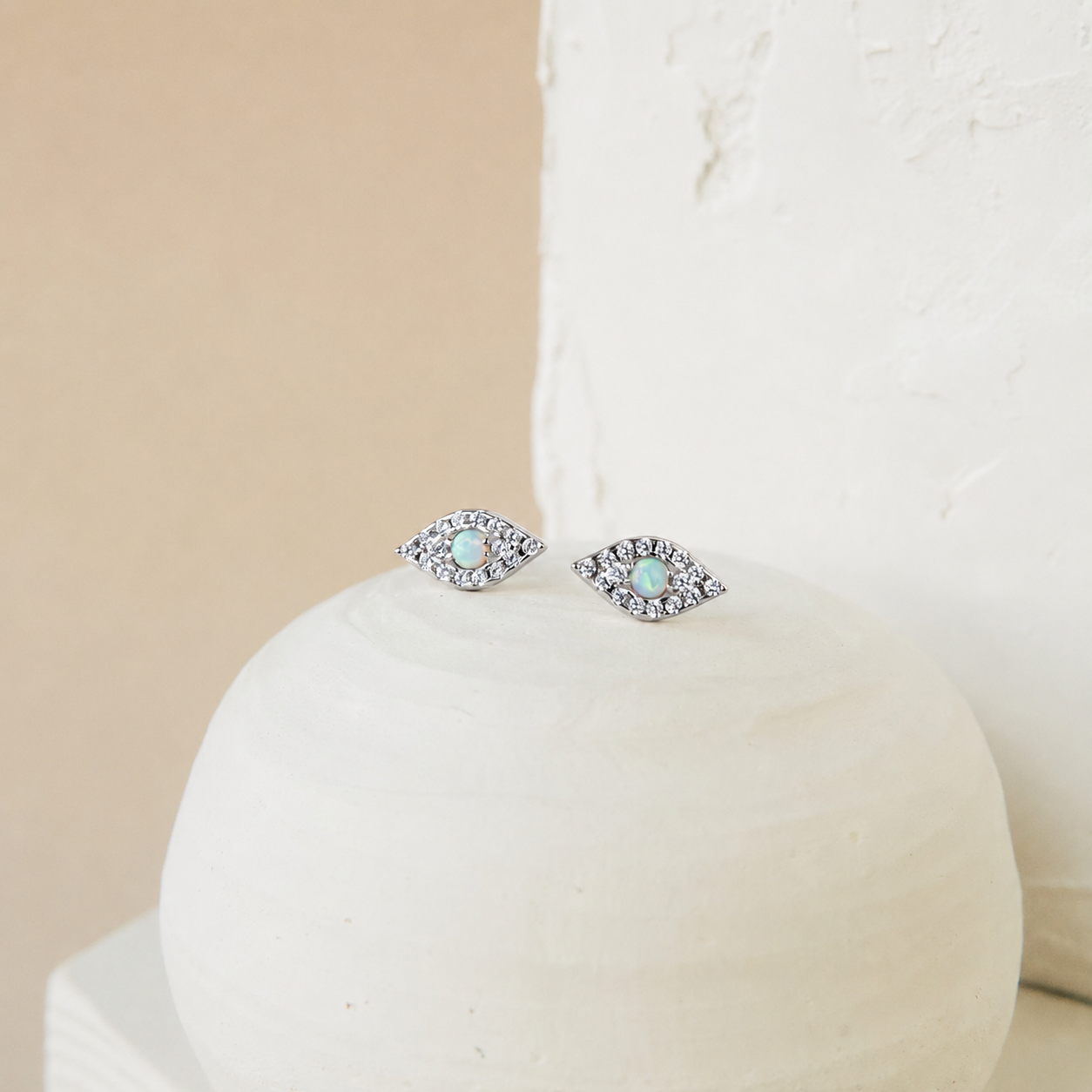 Pair of silver earrings with gemstones on a white stand against a beige background