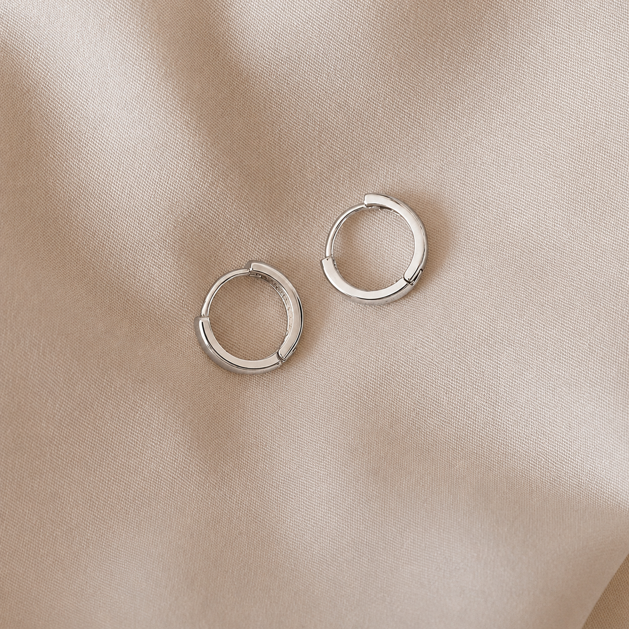 Pair of silver hoop earrings on a beige fabric background