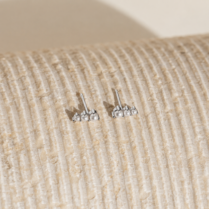 Pair of silver stud earrings on a textured beige surface