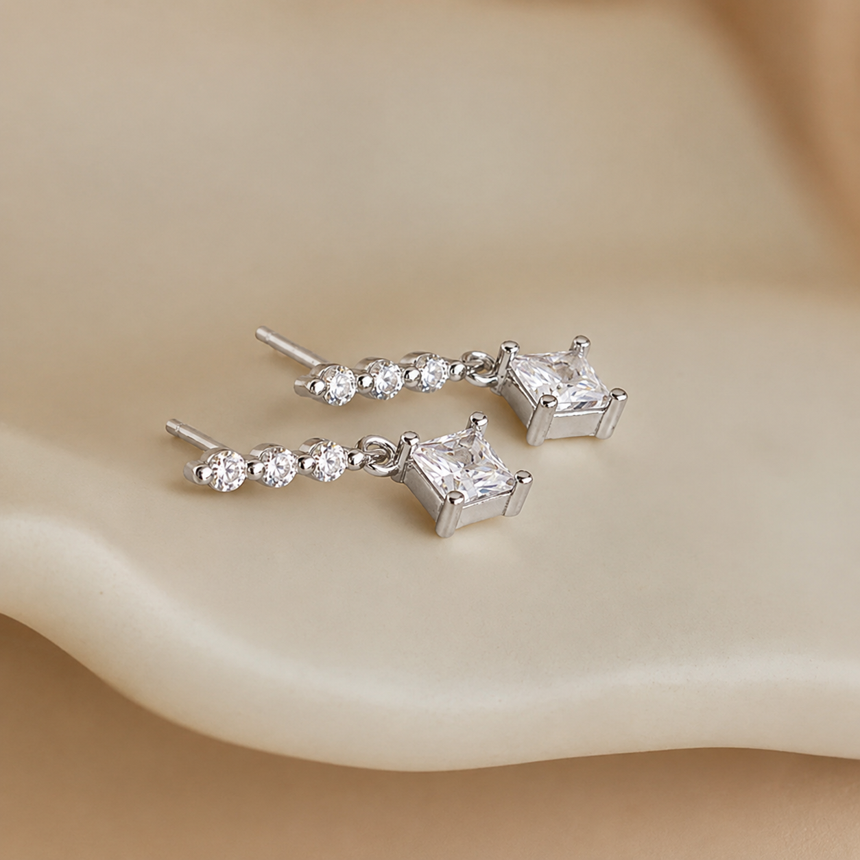 Silver earrings with clear gemstones on a beige surface