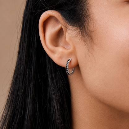 Close-up of an ear wearing a silver hoop earring with a neutral background