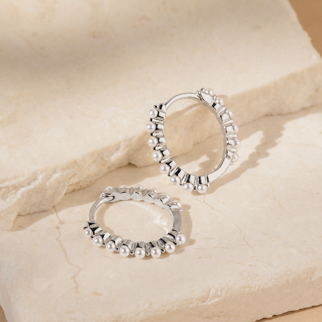 Silver hoop earrings on a beige stone surface