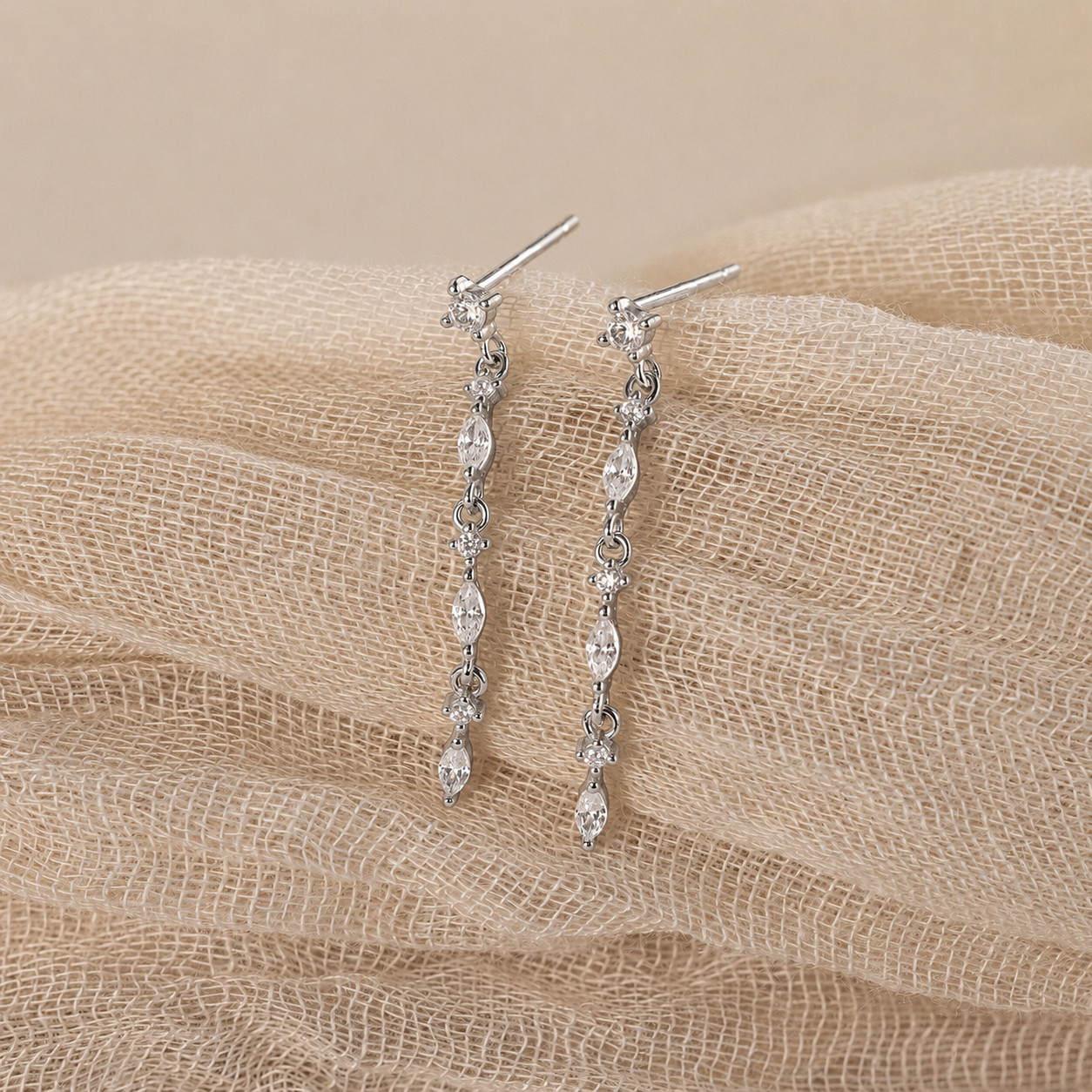 Silver earrings with clear stones on a beige fabric background