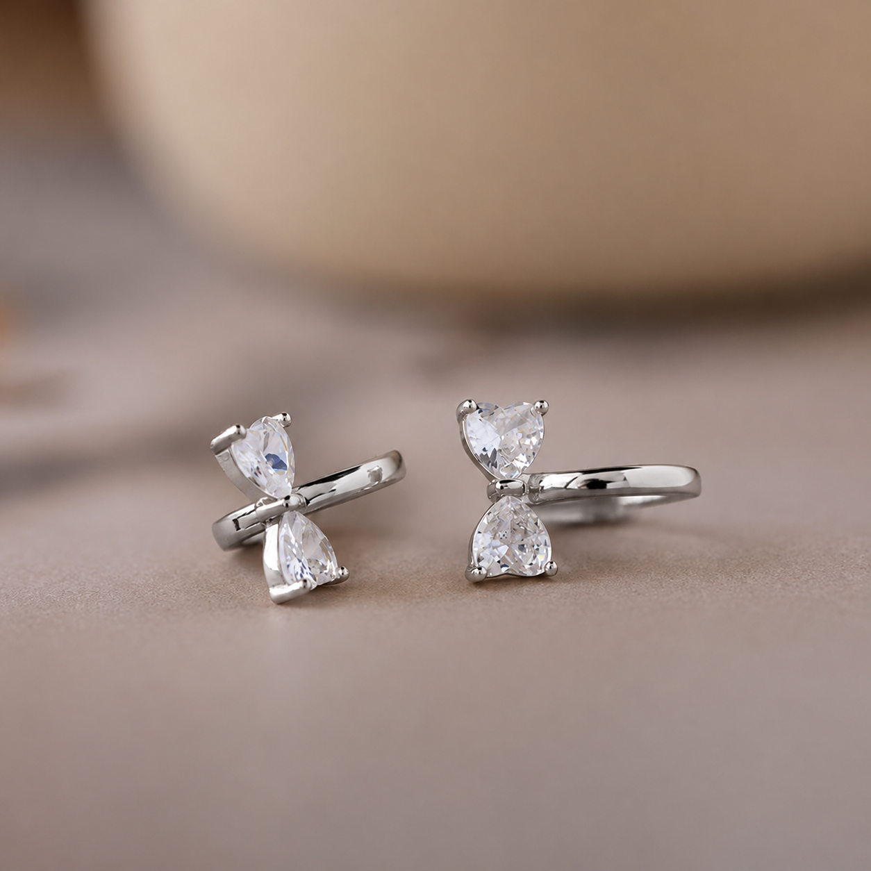 Silver bow-shaped earrings with clear gemstones on a beige surface