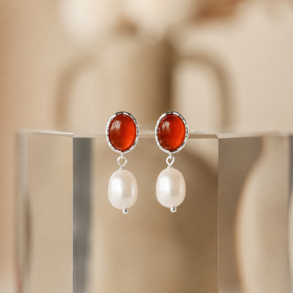 Pair of earrings with red gemstones and pearl drops on a neutral background