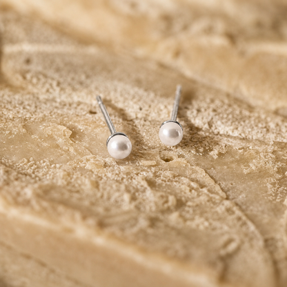 Pair of pearl stud earrings on a textured beige surface
