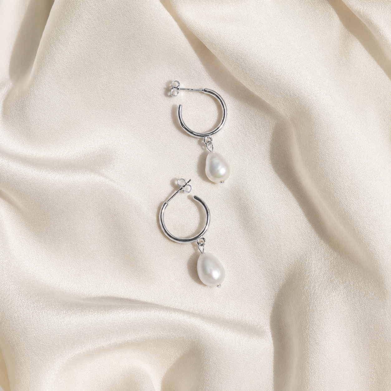 Silver hoop earrings with pearl drops on a beige fabric background