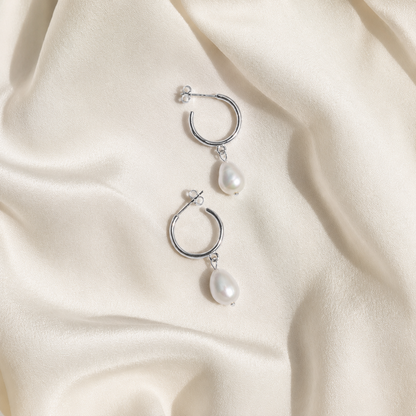 Silver hoop earrings with pearl drops on a beige fabric background