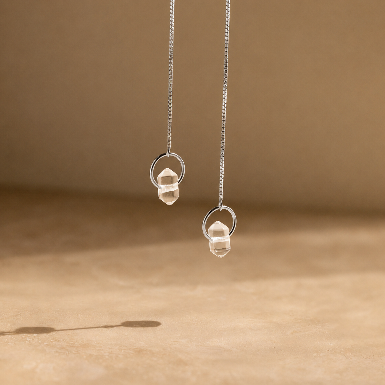 Silver earrings with clear stones on a beige background