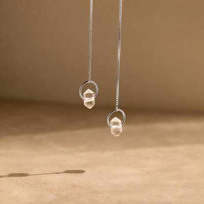 Silver earrings with clear stones on a beige background