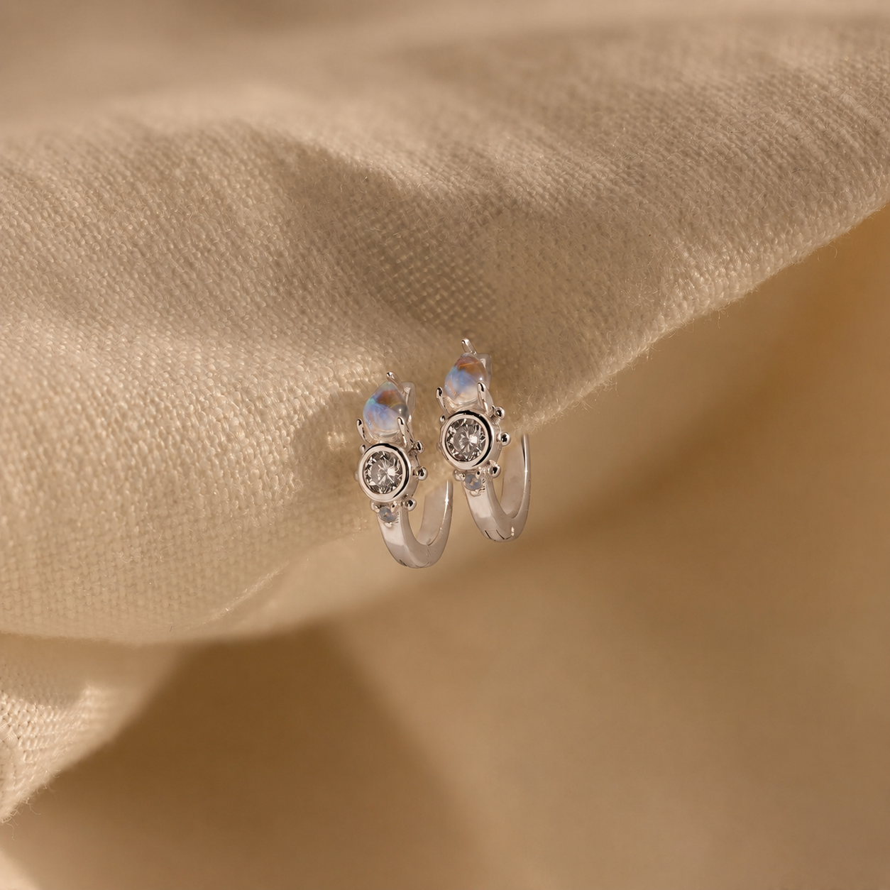 Silver hoop earrings with gemstones on a beige fabric background
